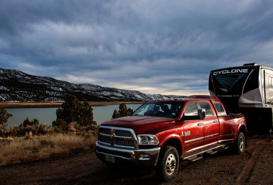 a red pickup truck tows an rv in front of a lake and snowy hills
