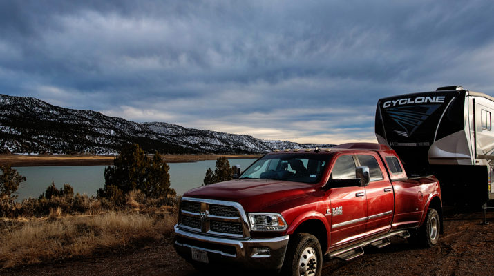 a red pickup truck tows an rv in front of a lake and snowy hills